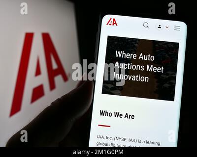 Persona in possesso di smartphone con pagina web della società di mercato auto USA IAA Inc. Sullo schermo di fronte al logo. Messa a fuoco al centro del display del telefono.