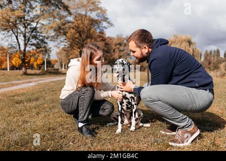 Una giovane coppia si diverte con un cane dalmata all'aperto. Foto Stock