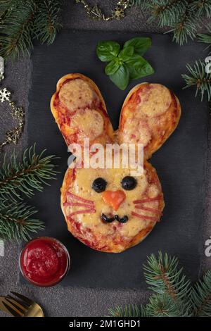 Deliziosa pizza al coniglietto con salsa di pomodoro, salame, formaggio, olio d'oliva, olive nere e basilico su piatto d'ardesia. Idea di cibo per il nuovo anno 2023 Foto Stock