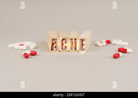 Concetto medico. Su una superficie grigia ci sono pillole e un blocco di legno rosso con l'iscrizione - ACNE Foto Stock