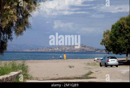 Lesbos - Anaxos spiaggia con coppia tenendo le mani a piedi lungo la costa. Molyvos città e castello in lontananza. Settembre / Ottobre 2022. Foto Stock