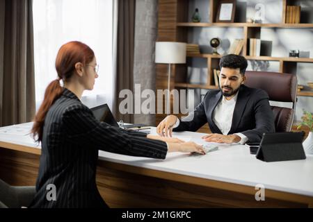 Businesswoman che offre lotto di cento dollari fatture al CEO maschio bearded. Donna d'affari che dà i soldi al suo socio. Uomo d'affari che riceve denaro da una donna d'affari. Venalità, corruzione, concetto di corruzione Foto Stock