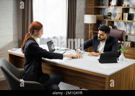 Giovane donna d'affari capelli rossi che dà un denaro illegale o denaro di tangente al suo commerciante d'affari portatore in ufficio. Tributo, soldi sporchi, concetto di tangente. Foto Stock