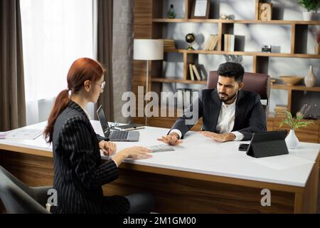 Giovane donna d'affari capelli rossi che dà un denaro illegale o denaro di tangente al suo commerciante d'affari portatore in ufficio. Tributo, soldi sporchi, concetto di tangente. Foto Stock