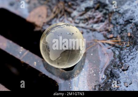 Concetto ambientale. Sfera di vetro - un pianeta che giace sulla griglia di una fossa di drenaggio per raccogliere l'acqua. L'acqua contaminata fluisce nello scarico. Foto Stock