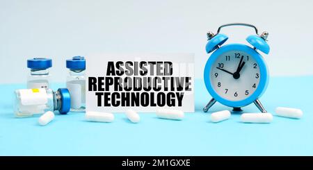 Medicina e concetto di salute. Un orologio di allarme, pillole, iniezioni e una scheda con l'iscrizione - Assisted Reproductive Technology Foto Stock
