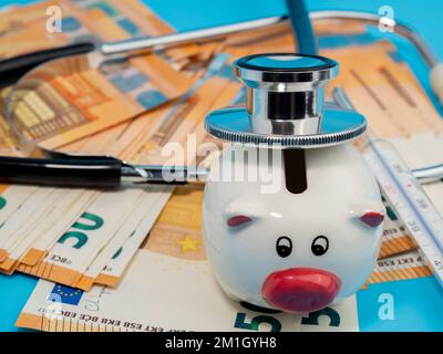 Stetoscopio medico, banco di porcellini, termometro e banconote su sfondo blu. Primo piano. Foto Stock