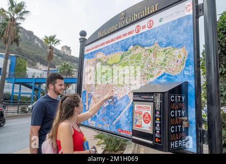 Gibilterra - giovane coppia allegra guardando una grande mappa di Gibilterra, e indicando la posizione di un'attrazione turistica al suo interno. Foto Stock