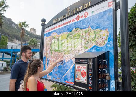 Gibilterra - giovane coppia allegra guardando una grande mappa di Gibilterra, e indicando la posizione di un'attrazione turistica al suo interno. Foto Stock