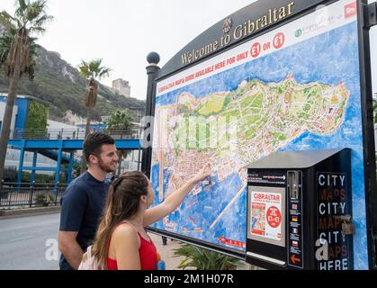 Gibilterra - giovane coppia allegra guardando una grande mappa di Gibilterra, e indicando la posizione di un'attrazione turistica al suo interno. Foto Stock