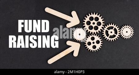 Concetto di business e finanza. Sulla superficie nera, frecce, ingranaggi e un'iscrizione - RACCOLTA FONDI Foto Stock