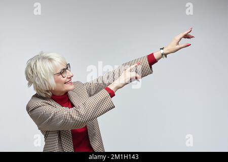 bella donna anziana con gli occhiali punta con il dito indice su un sedile vuoto. concetto di pubblicità di una donna leader di affari. Foto Stock