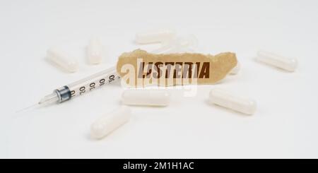 Medicina e concetto di salute. Su una tavola bianca ci sono pillole, una siringa e un pezzo di carta con l'iscrizione - Listeria Foto Stock