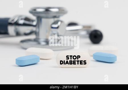 Medicina e concetto di salute. Su una superficie bianca si trovano pillole, uno stetoscopio e una compressa con l'iscrizione - Stop Diabetes Foto Stock