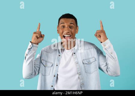 Allegro bel giovane afro-americano eccitato in casual con bocca aperta che mostra le dita in su Foto Stock