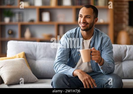 Ritratto di un bell'afro-americano che riposa sul divano con una tazza di caffè Foto Stock