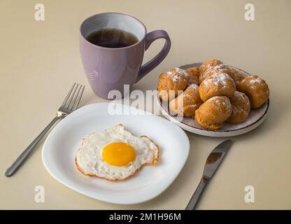 Colazione con uova fritte, una tazza di tè e profiteroles Foto Stock