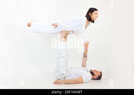 Adatta la famiglia su sfondo bianco. Uomo di mezza età sdraiato, tenendo con le gambe giovane donna equilibrante, pratica acroyoga. Foto Stock