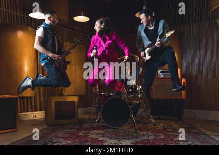 Rock band jumping. Due chitarristi e un cantante che saltano in alto nell'aria all'interno del loro studio garage. Scatto interno a lunghezza intera. Foto di alta qualità Foto Stock