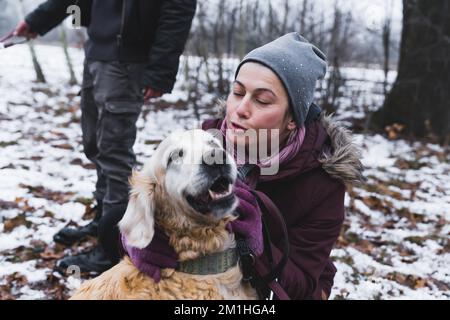 Volontario riparo cane. Donna caucasica di mezza età che dà un bacio per proteggere il cane - riprovatore d'oro di razza mista. Ritratto all'aperto. Neve a terra. Foto di alta qualità Foto Stock