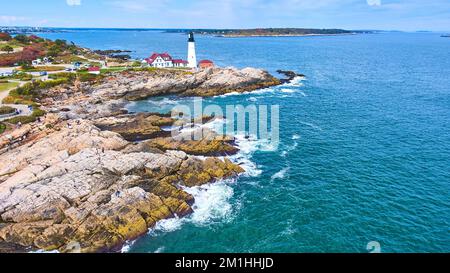 Splendida vista aerea sulle coste rocciose del Maine con onde che si infrangono e faro bianco Foto Stock