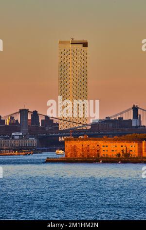 Grattacielo di Lone e Governors Island con Manhattan e i ponti di Brooklyn dall'acqua nell'ora d'oro di New York Foto Stock
