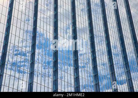 Dettaglio di un enorme grattacielo di vetro che riflette il cielo blu e le nuvole Foto Stock