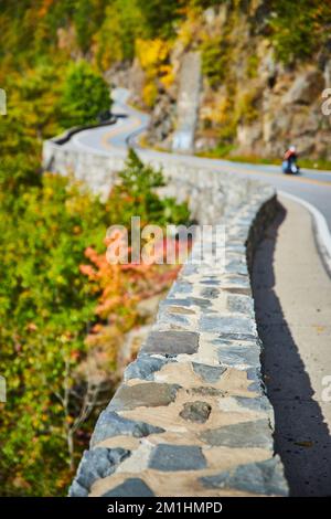 Parete di pietra e strada che si snoda attraverso le scogliere di montagna con ciclisti che attraversano e si concentrano sul primo piano Foto Stock