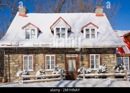 Vecchio 1826 Canadiana cottage stile fieldstone casa con tetto in lamiera rossa in inverno. Foto Stock