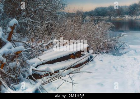 in inverno, la barca capovolta sulla riva del fiume Foto Stock