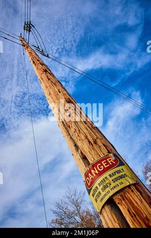 Guardando in su al palo del telefono con grande cartello DI PERICOLO postato circa l'area di inondazione Foto Stock