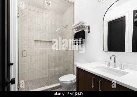 Un bagno con un mobile da toletta in legno e una doccia marrone piastrellata. Foto Stock