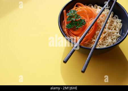 tagliatelle di ramen vegetariane con bacchette su sfondo giallo Foto Stock