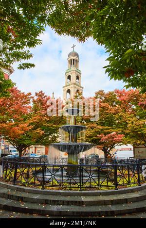 Splendida fontana circondata da foglie autunnali in città con Chiesa cristiana campanile dietro a New York City Foto Stock