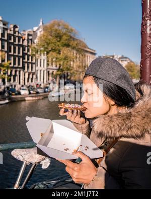 Le donne asiatiche con uno Stroopwafel ad Amsterdam sono tipici piatti olandesi due pezzi circolari di waffle riempiti con uno sciroppo di caramello Foto Stock