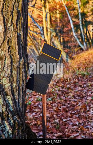 Primo piano dei pannelli solari portatili di carica per telefono ottenere la luce solare da albero in tardo autunno con fogliame Foto Stock