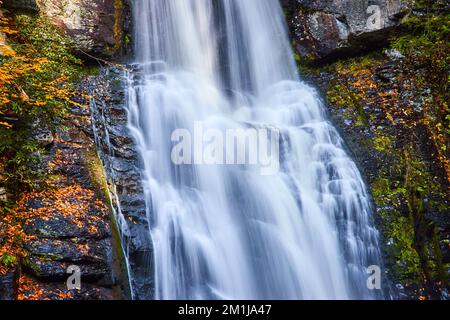 Da vicino alla rampicante cascata con sfocatura del movimento sulle scogliere e le foglie dorate che ricoprono le rocce Foto Stock