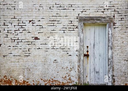 Abbandonato edificio in mattoni bianchi con vecchia porta in legno decadente e lichen Foto Stock
