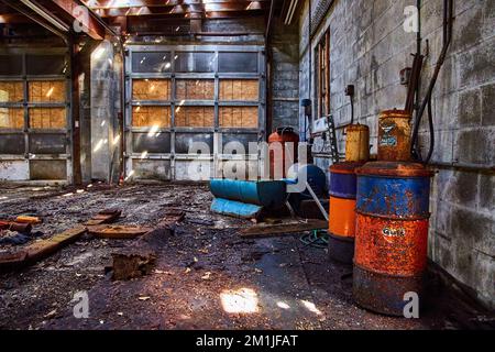 Interno abbandonato officina meccanica con terreno sporco e vecchie botti di lubrificante Foto Stock