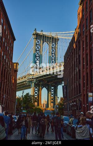 Edifici in mattoni e turisti incorniciano la vista del soleggiato Ponte di Manhattan a Brooklyn da vicino Foto Stock