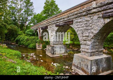 Vecchio ponte ad arco in pietra per binari ferroviari sul piccolo fiume Foto Stock