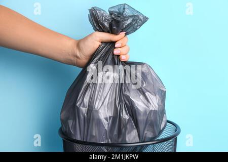 Donna che prende il sacchetto di immondizia dal bidone di immondizia sullo sfondo di colore, primo piano Foto Stock