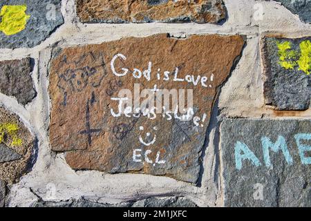 Dettaglio giù su pietra graffiti parete Dio è amore Gesù è vita sorridente faccia Foto Stock