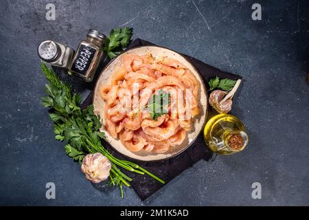 Dieta di cottura sfondo bianco di carne di pollame. Strisce di pollo fresche a fette crude per la cottura, con spezie, erbe aromatiche, su uno sfondo di cemento nero vista dall'alto c Foto Stock