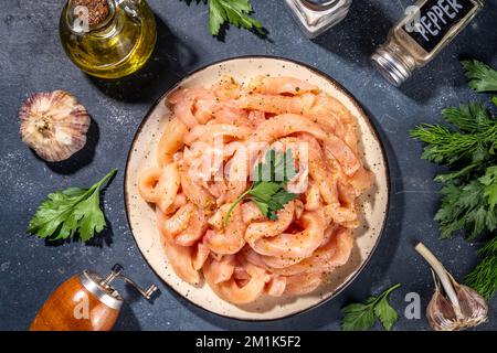 Dieta di cottura sfondo bianco di carne di pollame. Strisce di pollo fresche a fette crude per la cottura, con spezie, erbe aromatiche, su uno sfondo di cemento nero vista dall'alto c Foto Stock