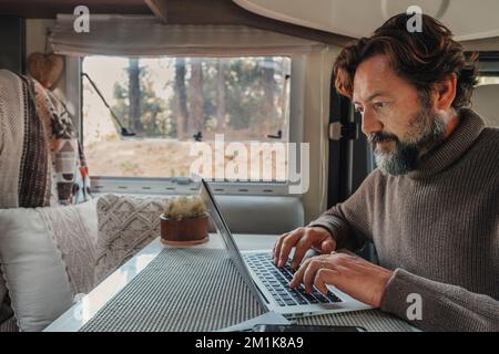 Un uomo che lavora su un computer portatile all'interno di un camper in un ufficio alternativo e in uno stile di vita professionale. Libertà nel lavoro intelligente. Nomade digitale van LIFE. Foto Stock