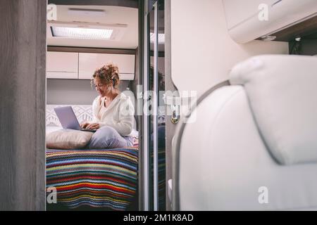 Una donna sola che lavora felice con il portatile e la connessione online seduto sul letto in camera camper van. Persone che lavorano libertà di viaggio stile di vita. Furgone lif Foto Stock