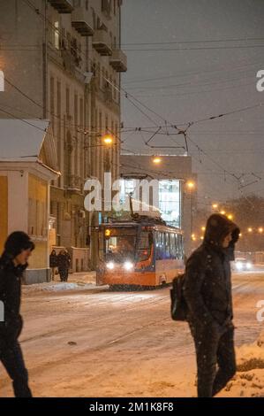 Mosca, Russia - 7 dicembre 2022: Persone che attraversano la strada vicino al tram. Il tram attraversa la città innevata d'inverno Foto Stock