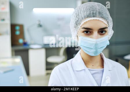 Ritratto di giovane donna che indossa maschera viso guardando la macchina fotografica in laboratorio medico, spazio copia Foto Stock