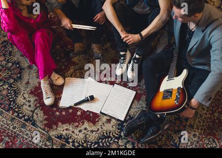 Ripresa ad angolo alto di quattro membri della band seduti accanto ai fogli di appunti su un tappeto a motivi. Cooperazione tra musicisti. Foto di alta qualità Foto Stock